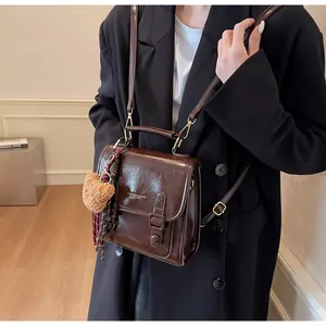 Detalle del bolso bandolera marrón brillante con colgante de oso y cinta de cuadros