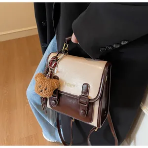 Detalle de bolso bandolera bicolor con colgante de oso de peluche y hebilla metálica