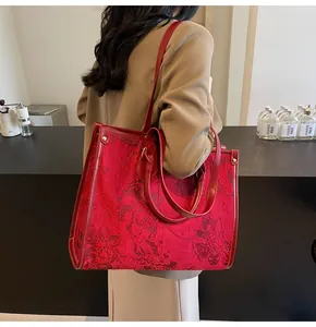 Detail of red floral jacquard tote bag with leather straps on a model in a cafe