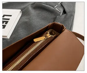 Detail of smooth golden metal zipper on a brown leather shoulder bag with striped lining