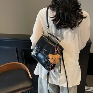 Bolso bandolera clásico de cuero sintético negro con colgante de oso en un entorno