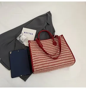 Detail view of the red houndstooth tote bag with leather handles and metallic rivet accents