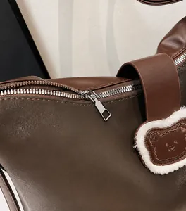 Detail of a brown leather bag showing a smooth zipper and a cute teddy bear charm