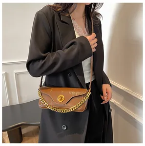 Detailed view of brown textured leather crossbody bag with bold gold chain and buckle