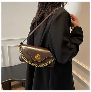 Detail of dark brown glossy baguette bag featuring a gold chain and wavy edge cover