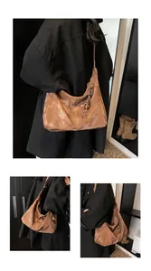 Detail view of brown leather crescent bag showing glossy marble texture and gold ring hardware