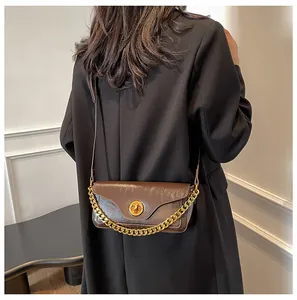 Detail of dark brown leather envelope bag with gold circular lock and thick metal chain