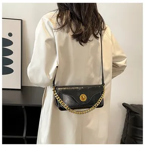 Rear view of a model wearing a black glossy leather bag with chunky gold chain