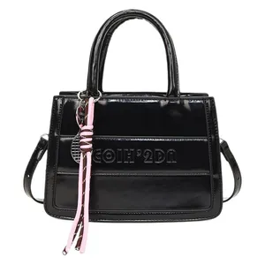 Glossy black patent leather tote bag with embossed letters and pink braided charm