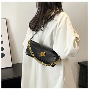 Black glossy leather shoulder bag with gold chain strap shown on a model's shoulder