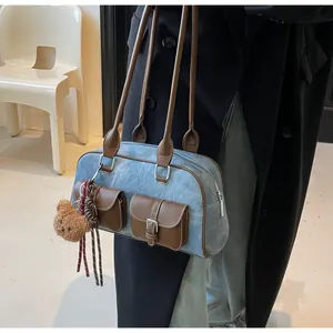 Detail of blue denim Boston bag with brown leather pockets and plush bear charm