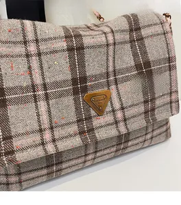 Detail of grey and pink checkered fabric bag with gold triangular metal logo plaque