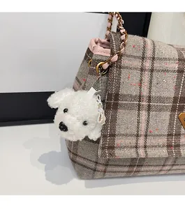 Detail of white plush dog charm with metal chain on a vintage brown checkered tote bag