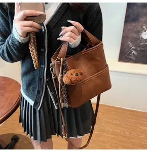 Close-up of brown bucket bag with decorative stitching and a plush teddy bear charm