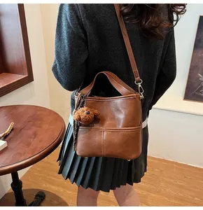 Detail of dark brown leather bucket bag with plush puppy charm and cross stitching detail