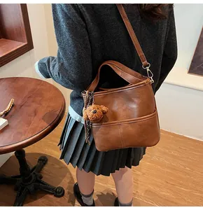 Close-up of brown PU leather bucket bag with cute plush puppy charm and fine stitching