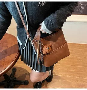 Detail of dark brown leather bucket bag with a cute plush teddy bear charm in front pocket