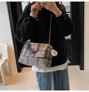 Detail of grey plaid tote bag featuring a metal triangle badge and chain shoulder strap