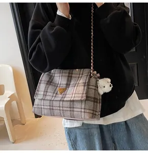 Detail of grey plaid wool crossbody bag with golden triangle clasp and plush charm