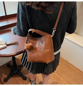 Detail showing deep brown faux leather bucket bag texture and plush bear pendant detail
