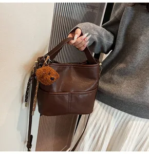 Detail of dark brown bucket bag with plush bear charm and striped scarf decoration
