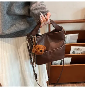 Detail of dark brown bucket bag featuring teddy bear charm and colorful woven cord