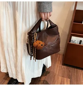 Detailed view of deep brown leather bucket bag with cute bear charm and woven rope accent