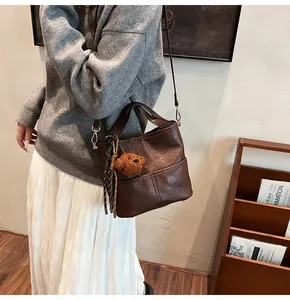 Detail of dark brown glossy bucket bag with plush bear charm and woven side knot detail