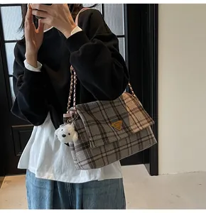 Detail of gray plaid tote bag with metallic triangle logo and white plush puppy charm