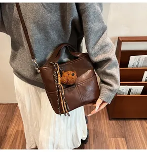 Detail of a dark brown matte leather bucket bag with a plush bear charm and woven tassel