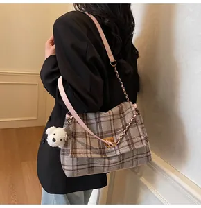 Detail of plaid tote bag with pink leather strap, metal chain, and cute plush dog charm