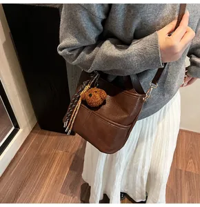Brown leather bucket bag detail with plush bear pendant and woven rope charm