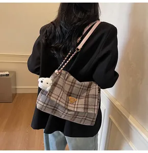 Detail of grey plaid tote bag featuring a plush dog charm and gold chain strap