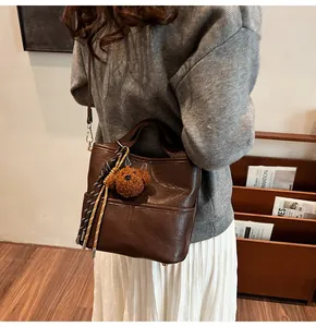 Detail of dark brown leather tote bag with a cute teddy bear charm and woven rope accent
