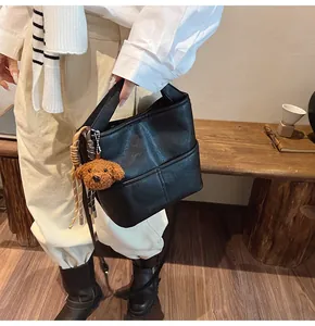 Close-up of black leather bucket bag featuring a cute brown teddy bear charm accessory