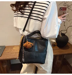Close-up of black leather bucket bag with dog plush charm and braided cord details