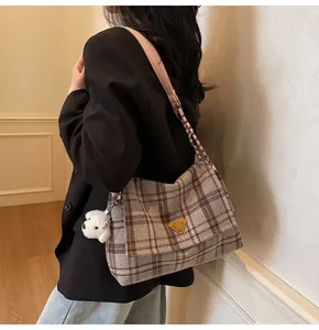 Detail of plaid tote bag featuring a pink strap, gold logo, and white dog plush pendant