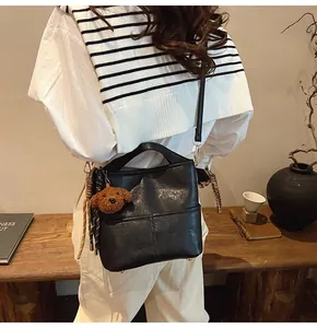 Detail of black faux leather bucket bag with plush bear charm on a warm wooden stand