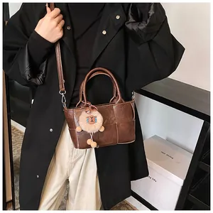 Détail du sac seau tressé marron foncé avec un charm lion en peluche et deux poignées