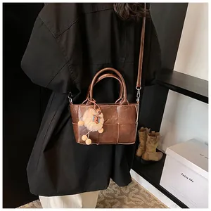 Détail du sac seau marron foncé tressé avec breloque lion en peluche et bandoulière amovible