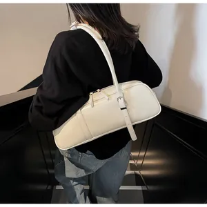 Detail view of cream baguette shoulder bag featuring silver zippers and adjustable strap