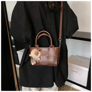 Détail du sac seau tissé à carreaux marron avec bandoulière et pendentif mouton en peluche