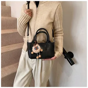Détail d'un sac seau tissé noir avec bandoulière réglable et breloque en peluche décorative