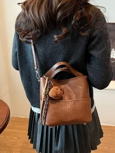 Brown leather bucket bag shown from behind on model with stylish bear charm accessory