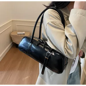 Detail of a black glossy baguette bag with silver buckles worn over a white trench coat