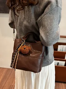 Minimalist dark brown leather bucket bag for women with cute teddy bear charm and strap