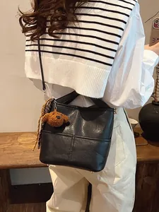 Chic black bucket bag with teddy bear charm shown in a casual lifestyle setting