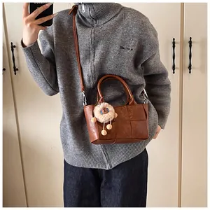 Détail d'un sac seau tressé marron avec texture en cuir PU et pendentif lion mignon