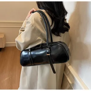 Detail view of a black glossy baguette shoulder bag styled with a beige coat in an indoor setting
