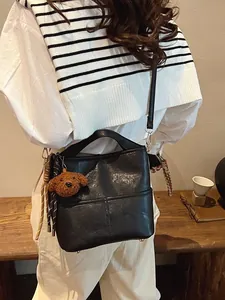 Minimalist black PU leather bucket bag with teddy bear charm and woven rope decoration